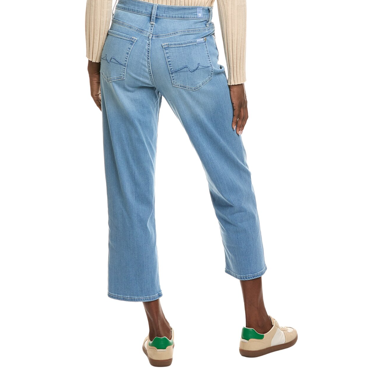 A person is wearing light blue cropped jeans with back pocket stitching, a beige ribbed sweater, and beige sneakers with green accents.