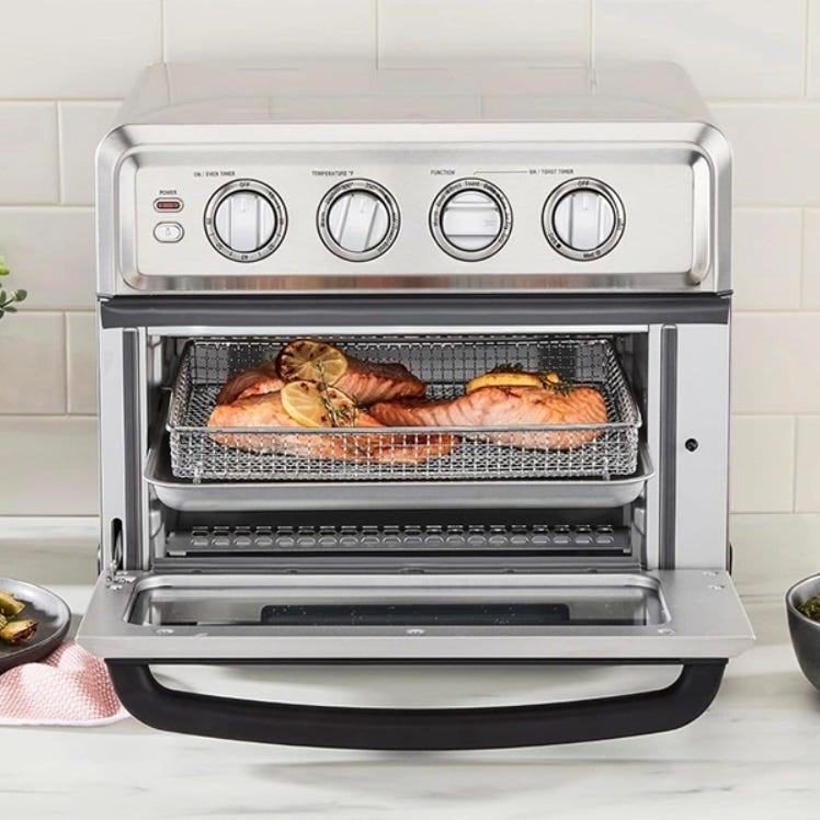 Countertop air fryer oven with two salmon fillets cooking on upper wire racks.