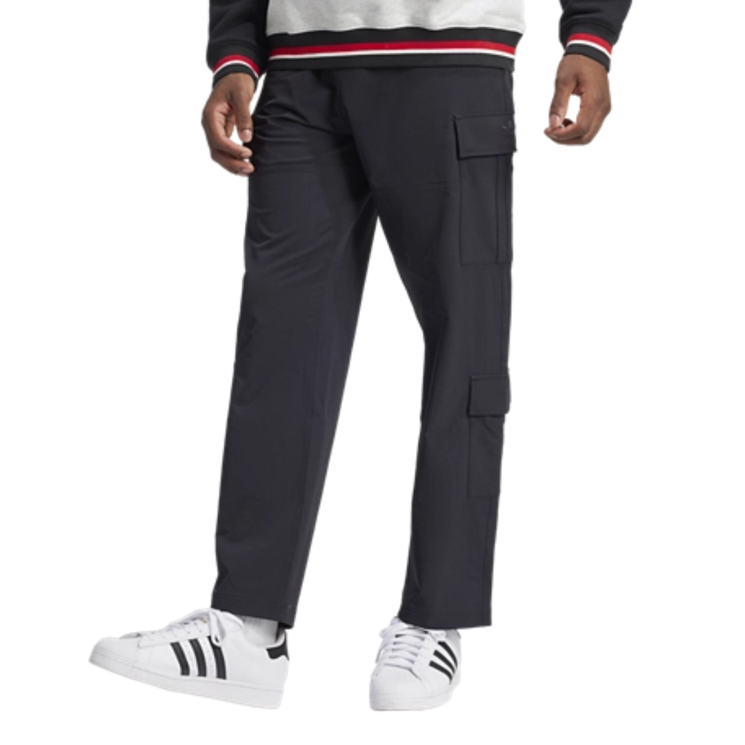 A person wearing black cargo pants with side pockets and white sneakers featuring black stripes, highlighted by a gray sweatshirt with red and white striped cuffs and waistband.