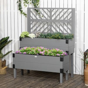 A two-tiered grey planter box filled with a variety of colorful flowers, set against a lattice backdrop and a white wall.
