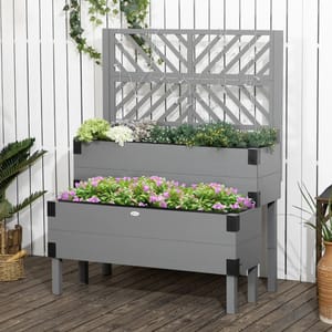 A two-tiered grey planter box filled with a variety of colorful flowers, set against a lattice backdrop and a white wall.