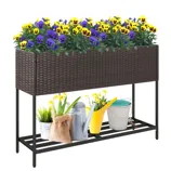 Rattan-style raised planter with purple and yellow flowers, featuring metal legs and a lower shelf. Includes gardening tools and supplies like a watering can and buckets on the shelf.