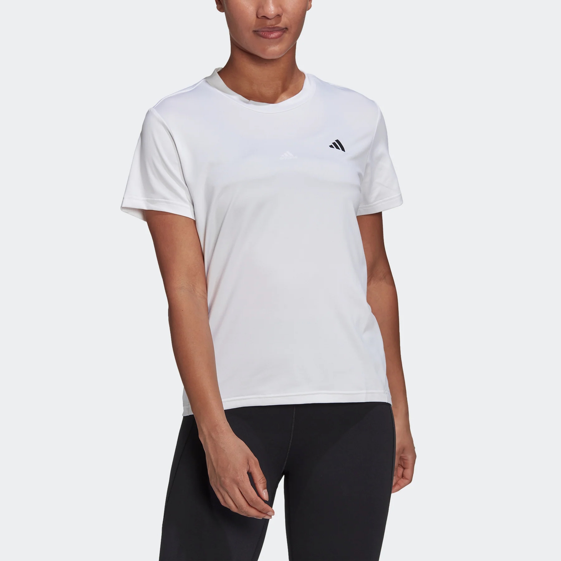A person wearing a white Adidas T-shirt with short sleeves and a crew neckline, paired with black leggings.