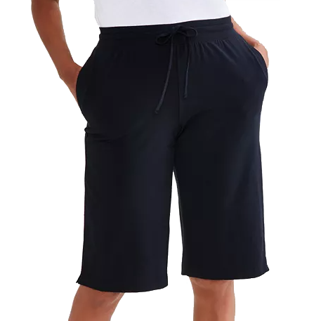 A person is wearing loose-fitting black shorts with an elastic waistband and drawstring, displaying a casual style with hands in the pockets.