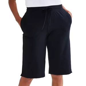 A person is wearing loose-fitting black shorts with an elastic waistband and drawstring, displaying a casual style with hands in the pockets.