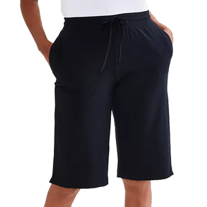 A person is wearing loose-fitting black shorts with an elastic waistband and drawstring, displaying a casual style with hands in the pockets.