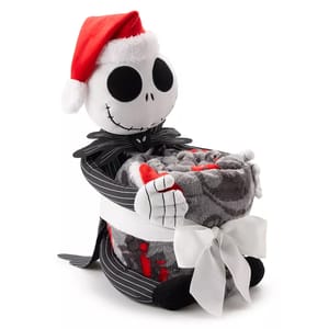 A plush Jack Skellington, wearing a Santa hat, holds a rolled-up grey and red throw blanket tied with a white ribbon.