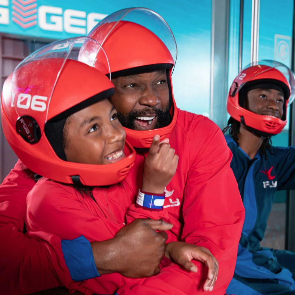 A group of people wearing red flight suits and helmets participate in an indoor skydiving experience at iFLY.