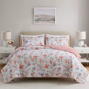 A bed with floral-patterned bedding and two matching pillowcases, complemented by a pink blanket. The setup includes two bedside tables with lamps and decorative items, set against a neutral wall with a landscape painting above the bed.