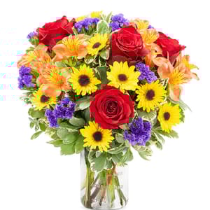 A vibrant bouquet of red roses, yellow sunflowers, orange alstroemeria, and purple statice in a clear glass vase.