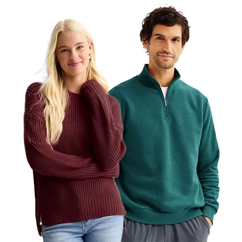 A man and a woman wearing casual winter clothing; the woman sports a burgundy sweater and jeans, while the man wears a teal quarter-zip pullover with dark pants.