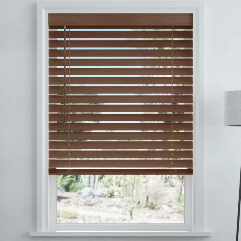 Brown horizontal window blinds partially open, with a view of a garden outside. White window frame and nearby light fixture visible.