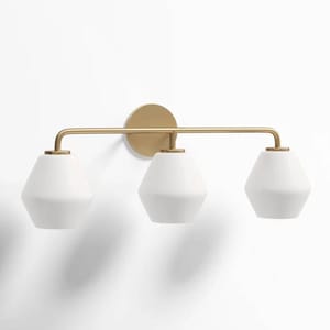 A modern vanity light featuring three geometric white shades with a sleek brass frame, mounted on a circular brass base. It's a dimmable fixture designed for stylish and functional lighting.