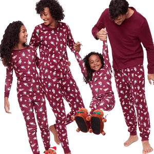 A family of four wearing matching maroon pajamas with festive prints, including reindeer slippers for one child and bundled feet for the others.