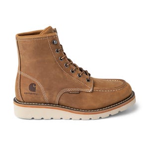 Carhartt Women's Moc-Toe Boots are tan, waterproof boots with white stitching, metal eyelets, and a white wedge sole. They feature the Carhartt logo on the heel and are designed for durability and comfort.
