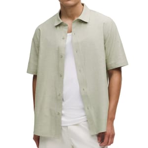 A person is wearing an open short-sleeve, light green button-up shirt over a white tank top, paired with light-colored pants.