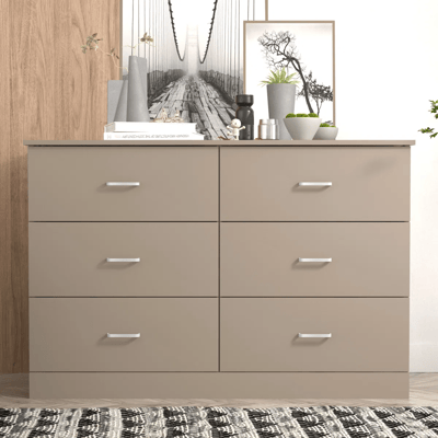 A six-drawer dresser in a neutral color is topped with books, decor items, plants, and framed artwork.