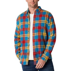 A man wearing a bright plaid shirt in blue, yellow, and red tones over a casual white t-shirt, paired with dark jeans.