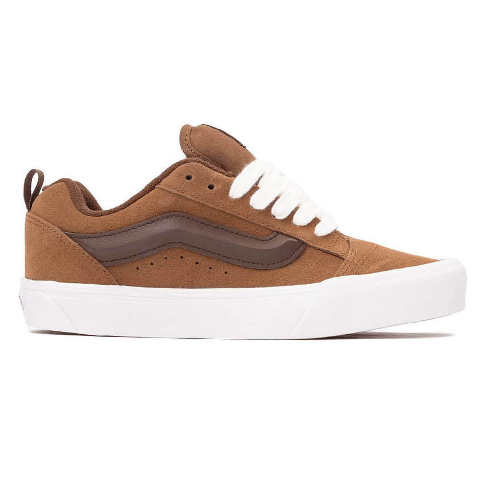 A brown and white low-top skate shoe with a suede upper, featuring a dark brown side stripe and white laces, set on a white rubber sole.