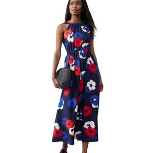 A woman is wearing a sleeveless navy blue dress with a large red, white, and blue floral pattern, holding a black clutch.
