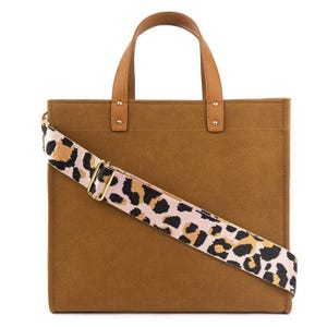 A brown tote bag featuring dual top handles and a wide pink shoulder strap with a leopard print pattern.