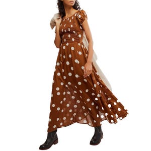 Brown polka dot maxi dress with short sleeves, paired with black ankle boots. A light-colored jacket is draped over one shoulder.