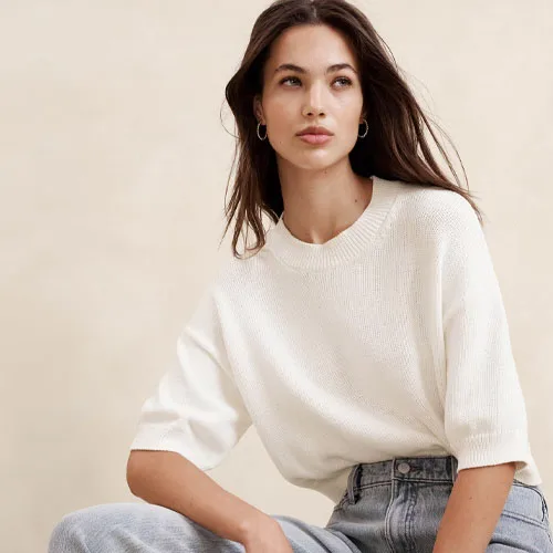 A woman wearing a white crewneck sweater and light blue denim jeans.