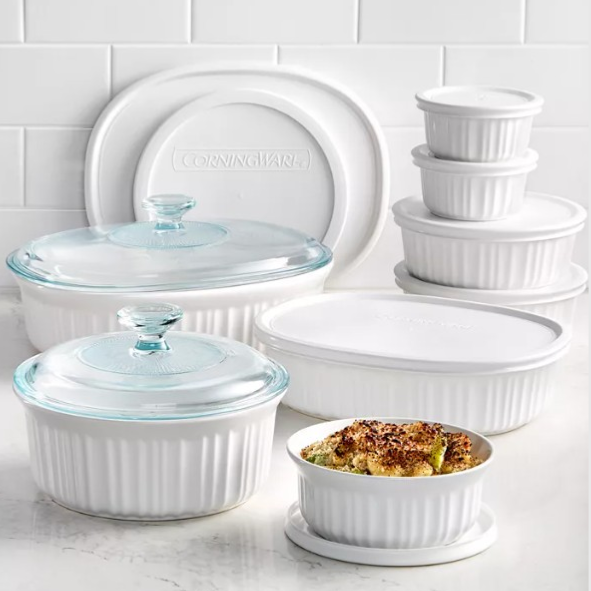 A set of white CorningWare dishes with varying sizes includes lidded casserole dishes and stackable containers. Some have glass lids, while others use plastic ones, and one dish holds a baked meal.