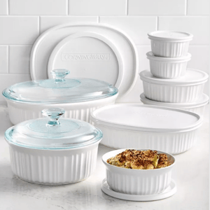 A set of white CorningWare dishes with varying sizes includes lidded casserole dishes and stackable containers. Some have glass lids, while others use plastic ones, and one dish holds a baked meal.