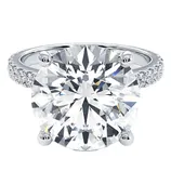 A round-cut diamond ring with a large center stone set in a four-prong setting, featuring a pavé diamond band on a silver or white gold metal.