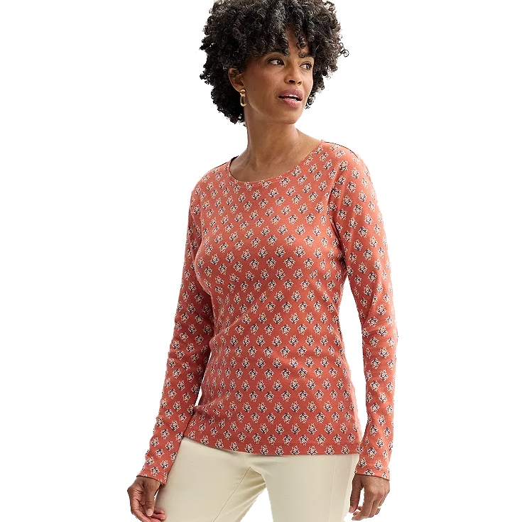 A woman is wearing a long-sleeve, patterned rust-colored top with small white floral designs and cream-colored pants.