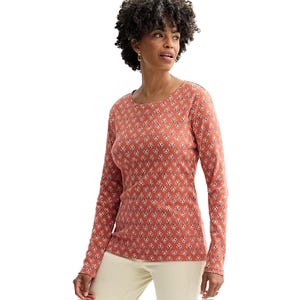 A woman is wearing a long-sleeve, patterned rust-colored top with small white floral designs and cream-colored pants.