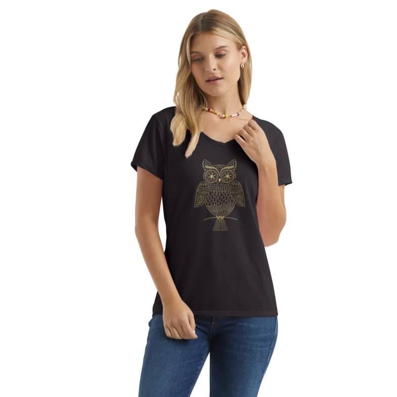 A woman is wearing a black T-shirt with a gold owl design on the front, paired with blue jeans and a colorful bead necklace.