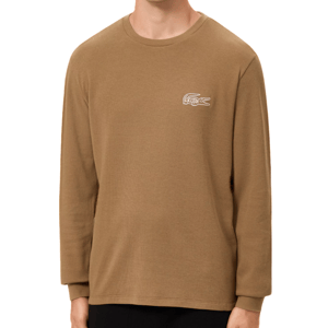 A man is wearing a brown Lacoste long-sleeve crew neck T-shirt with a white logo on the chest. The shirt is paired with black pants.