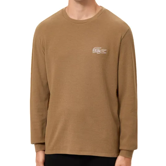 A man is wearing a brown Lacoste long-sleeve crew neck T-shirt with a white logo on the chest. The shirt is paired with black pants.