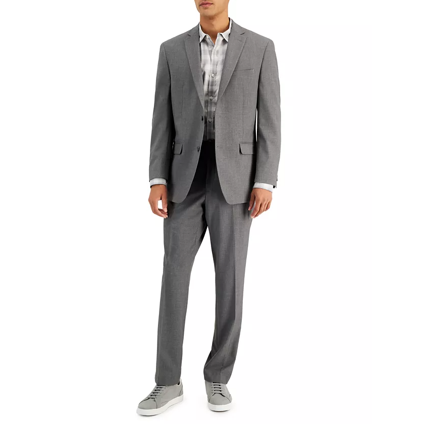 A man is wearing a light gray suit with a plaid dress shirt and gray sneakers. The outfit combines formal and casual elements.
