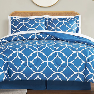 Blue and white geometric-patterned bedding set with two matching pillow shams on a bed with a wicker headboard.