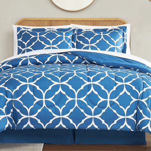 Blue and white geometric-patterned bedding set with two matching pillow shams on a bed with a wicker headboard.
