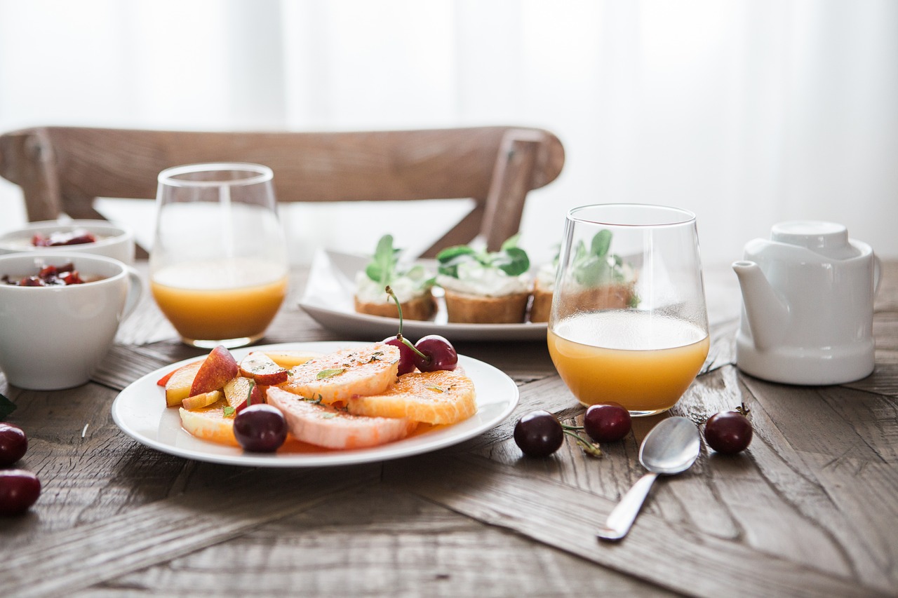 A breakfast setting with orange juice, toast with toppings, a bowl of yogurt with fruit, cherries, and a teapot.