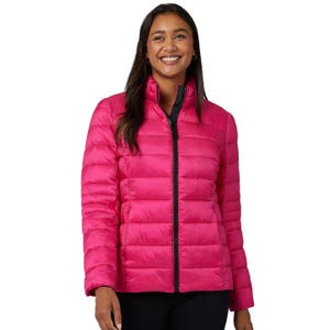 A woman is wearing a vibrant pink, lightweight, quilted packable jacket from 32 Degrees. The jacket has a high collar and a black zipper, ideal for layering and travel.