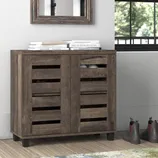 Wooden shoe cabinet with slatted doors, approximately 31.5'' H. Topped with books, it stands beside a window and some boots, with a decorative mirror above.