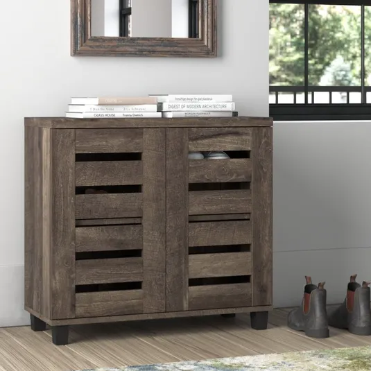 Wooden shoe cabinet with slatted doors, approximately 31.5'' H. Topped with books, it stands beside a window and some boots, with a decorative mirror above.