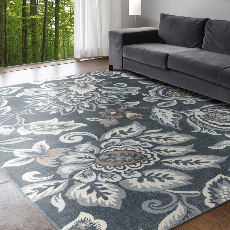 A patterned area rug on the floor with a gray sofa on its edge, beside a window with a forest view.