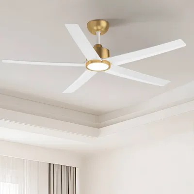 A modern ceiling fan with a gold and white finish, featuring five blades and an integrated light fixture, installed in a well-lit room with a tray ceiling and curtains.