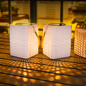 Two illuminated solar-powered LED lanterns with perforated designs casting patterns on a wooden surface during evening time.