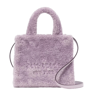 The Kate Spade Ellie Faux-Fur Small Tote is a soft purple handbag featuring plush faux-fur material with embossed branding on the front. It includes short handles and a detachable crossbody strap for versatile carrying options.