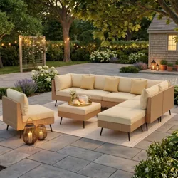 Outdoor seating set with a beige modular sectional, a matching chair, and a coffee table on a paved patio with string lights, plants, and lanterns for ambient lighting.