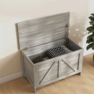 A gray wooden storage bench with its lid open, revealing a black and white patterned cushion inside.