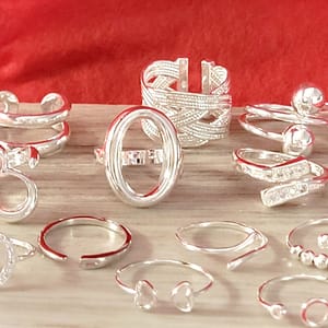 Assorted silver rings of various designs on a wooden surface with a red background.
