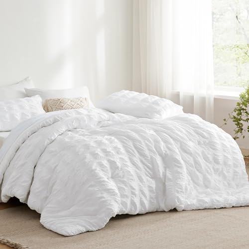 A white seersucker comforter set is displayed on a bed, with textured stripes providing a ruffled look. The set includes matching pillow shams behind a decorative pillow.